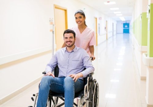 smiling-orderly-pushing-discharged-mid-adult-patient-wheelchair-corridor-hospital_662251-3081